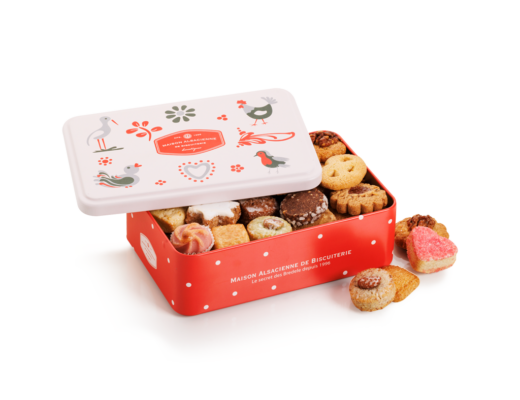 Une boîte rectangulaire décorée d'oiseaux et de motifs floraux est ouverte, révélant un assortiment de petits biscuits. La boîte est rouge à pois blancs, et quelques biscuits sont disposés à côté.